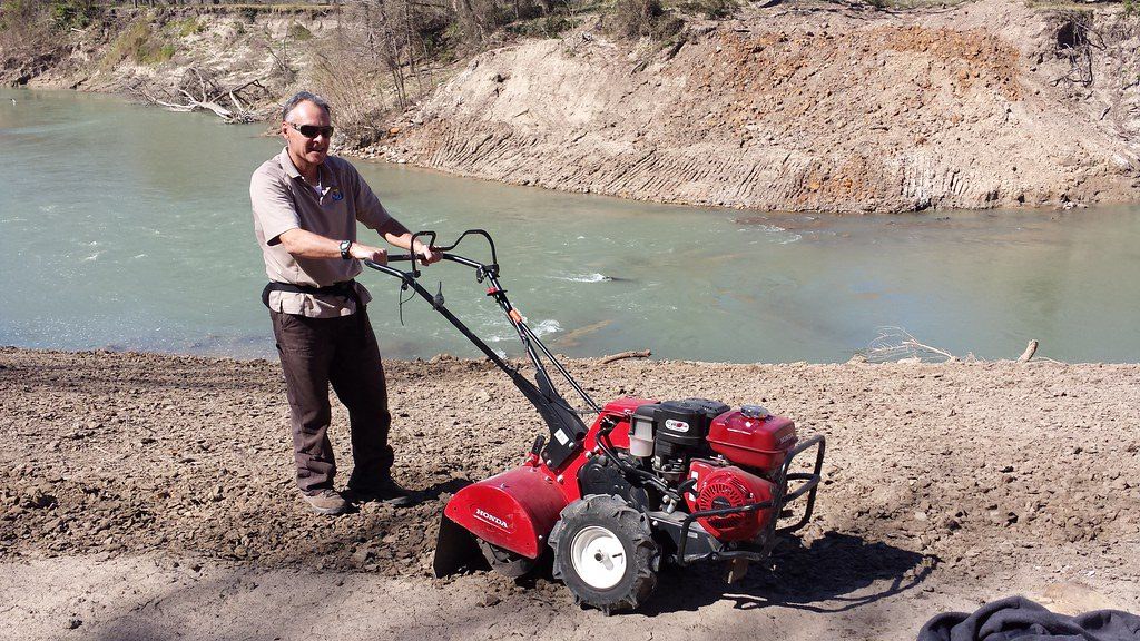 Worker running a rear-tine rototiller