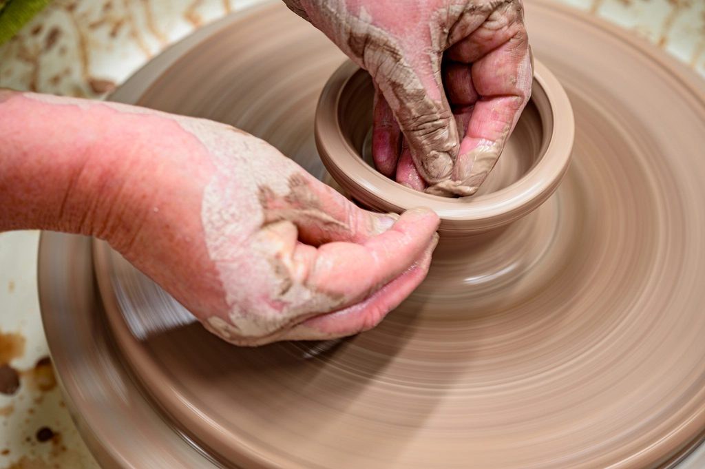 Hands shaping a clay bowl on a pottery wheel